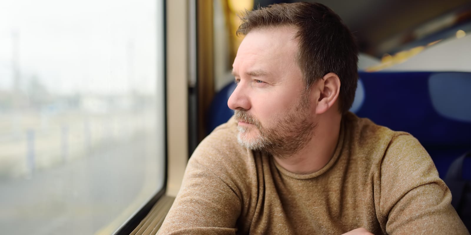 A man sitting by a train window, looking out at the view