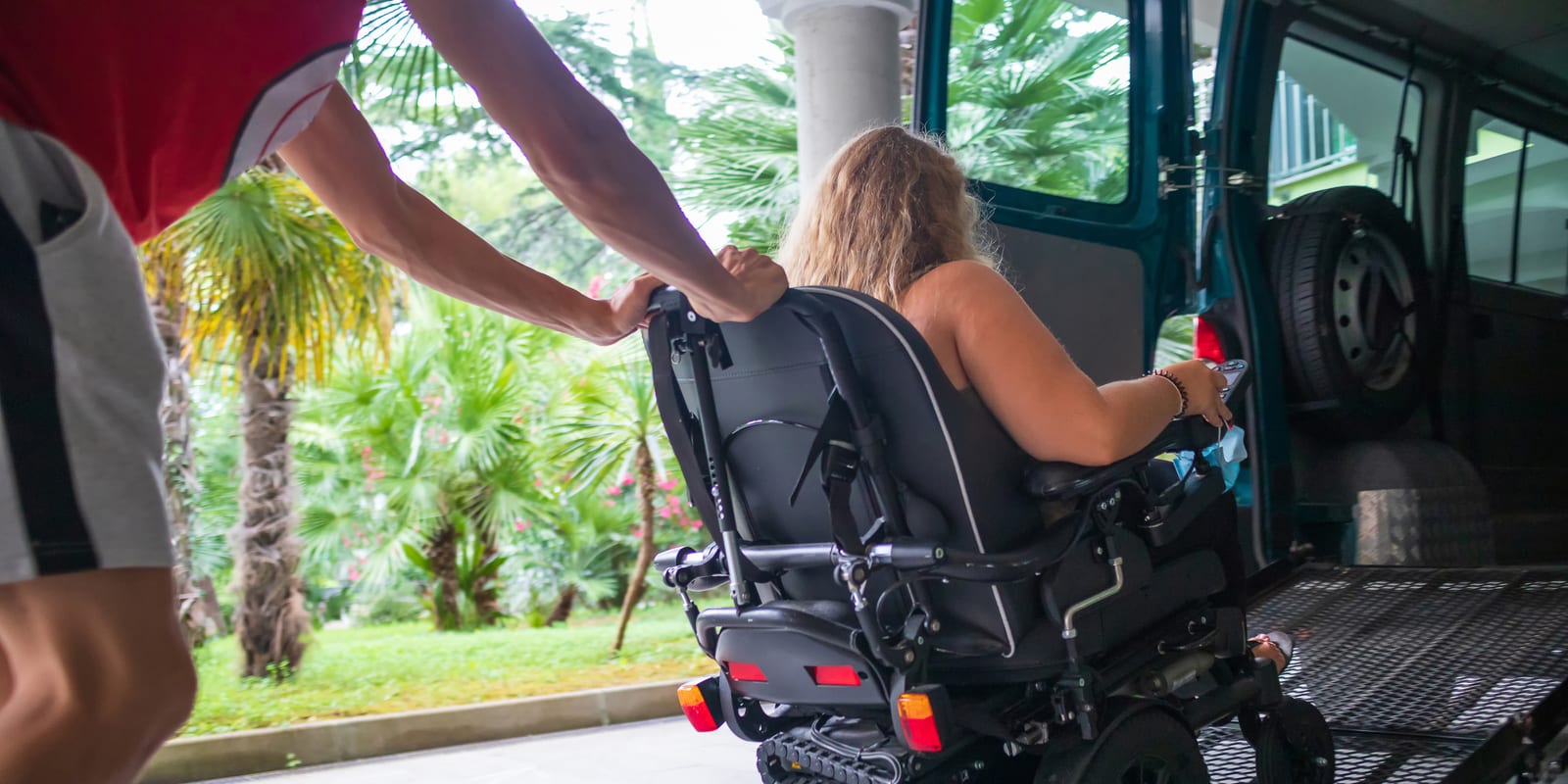 A support worker helping a woman in a power wheelchair onto the ramp of an accessible van