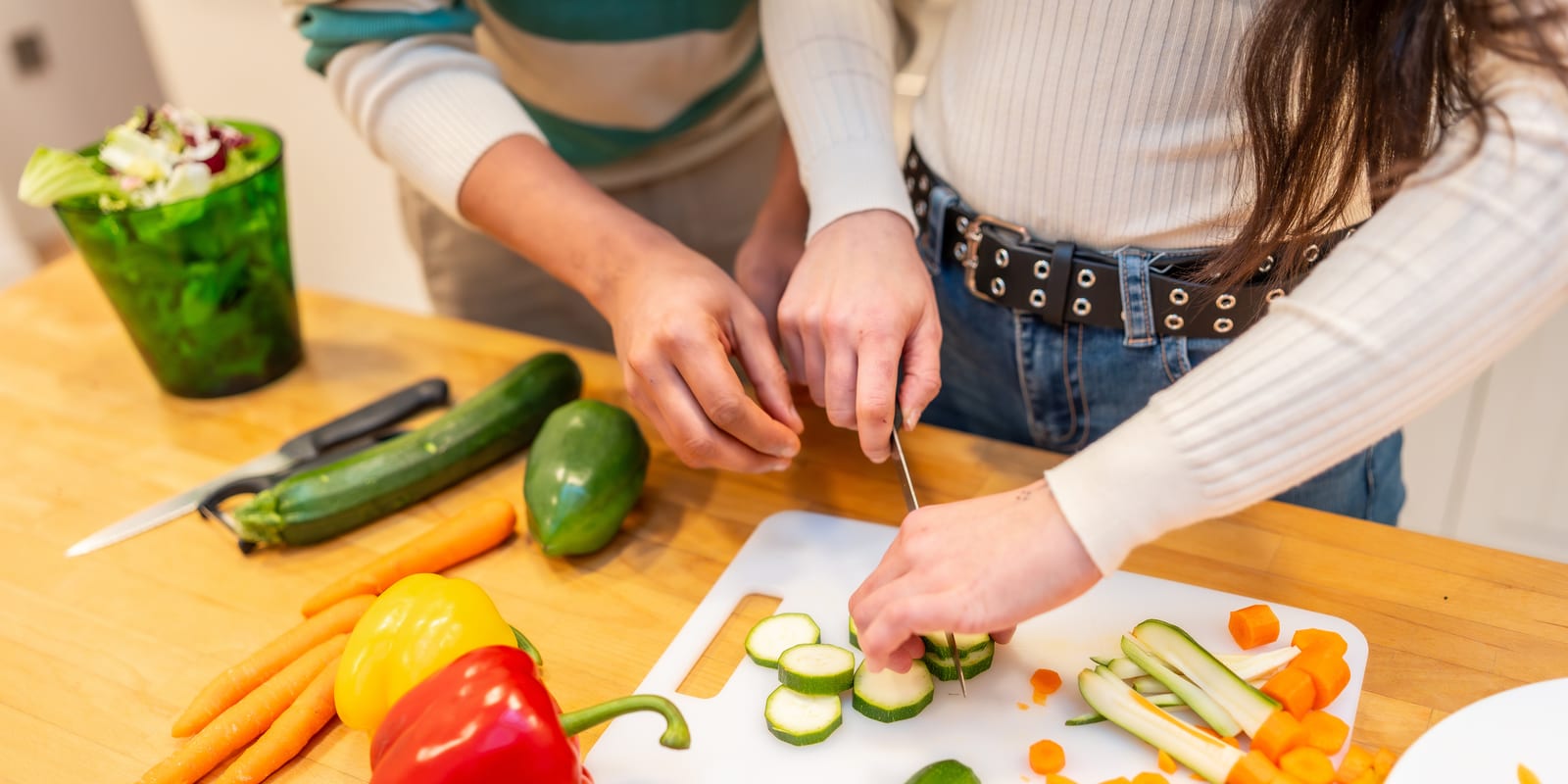 Two people preparing lunch together at a kitchen bench, one slicing zucchini on a chopping board