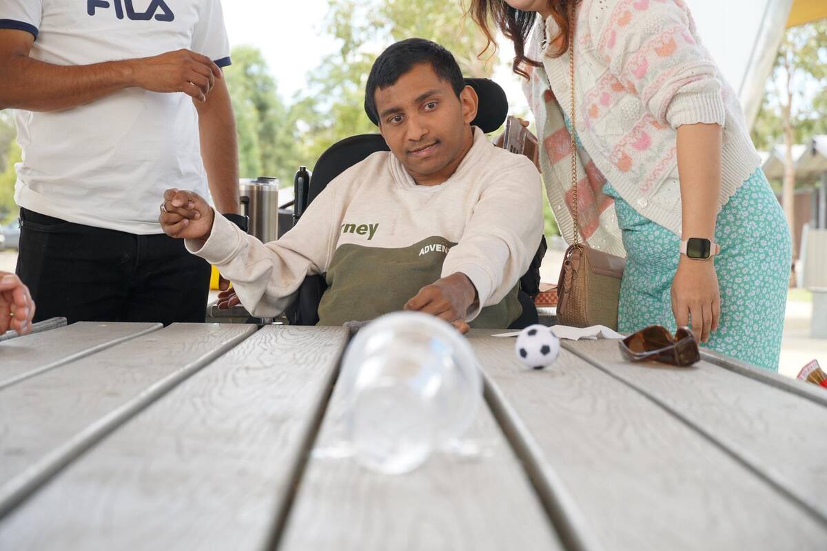 Enable Hub participant using a wheelchair playing a table game with support workers at a picnic table